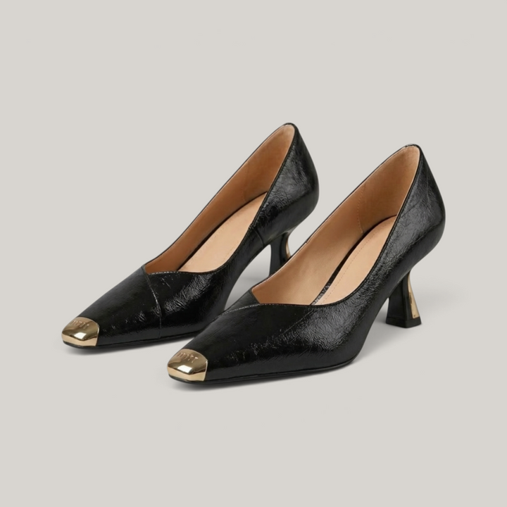 Black high-heeled shoes with gold toes on a gray background