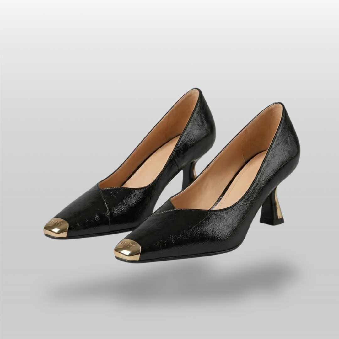 Black high-heeled shoes with gold toes on a gray background