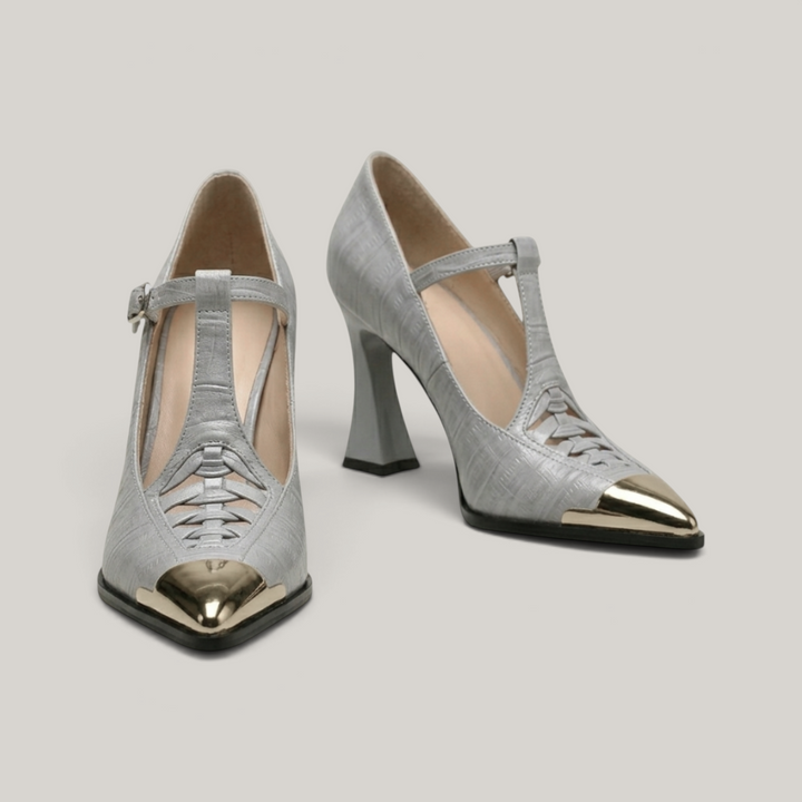 Pair of silver high-heeled shoes with gold toes on a light gray background