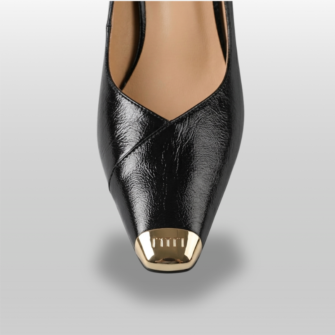 Black high-heeled shoe with gold cap toe on a gray background