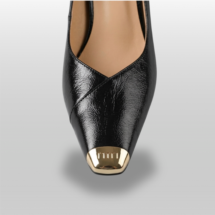 Black high-heeled shoe with gold cap toe on a gray background