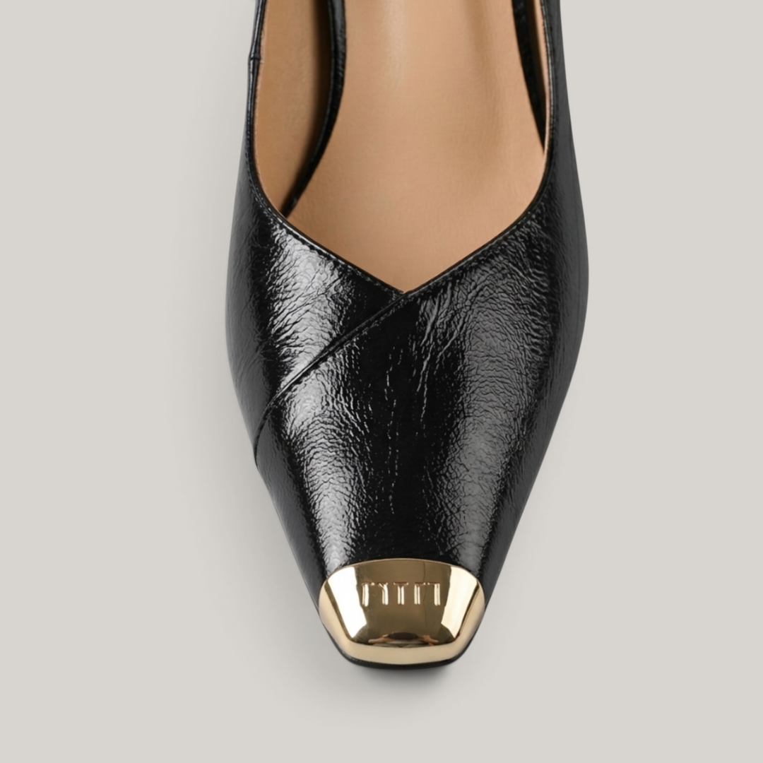 Black high-heeled shoe with gold cap toe on a gray background