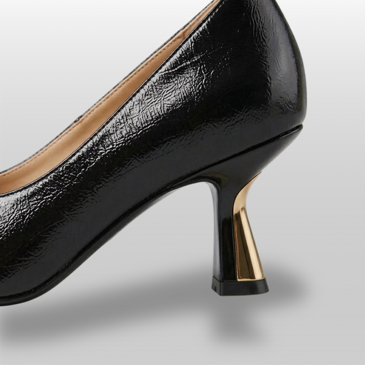 Black high-heeled shoe with gold heel on a light gray background