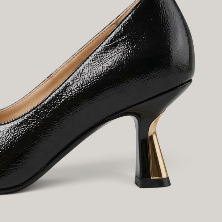 Black high-heeled shoe with gold heel on a light gray background