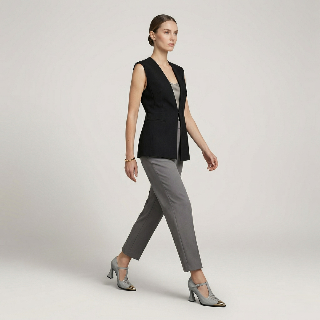 Woman wearing a black vest over a gray top and pants on a light gray background