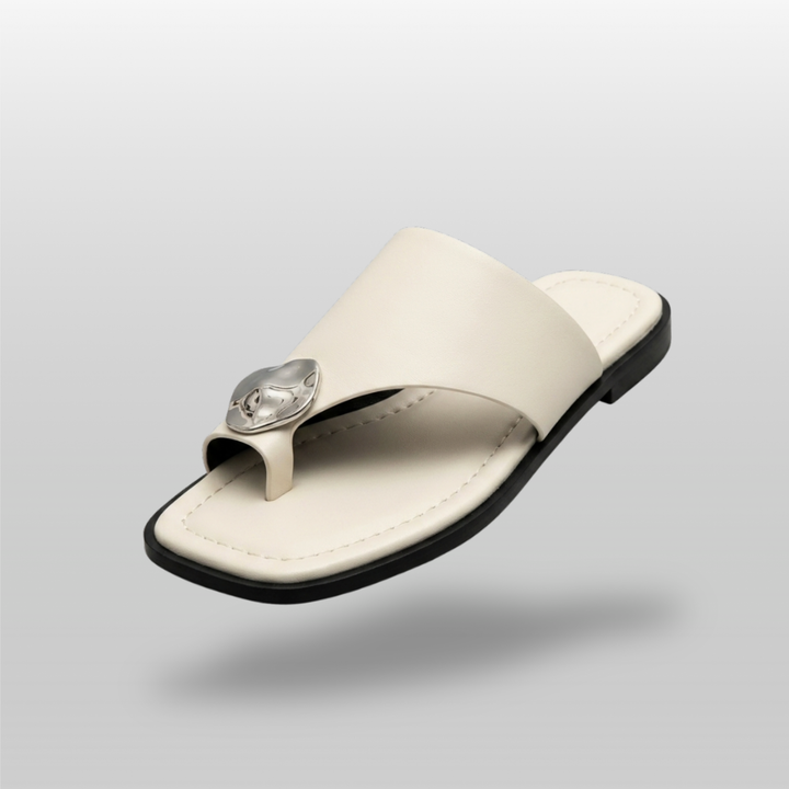 Cleo Sandal in Ivoire Argenté. Single wide ivory leather band, molten silver medallion, toe-ring thong construction on flat black sole.