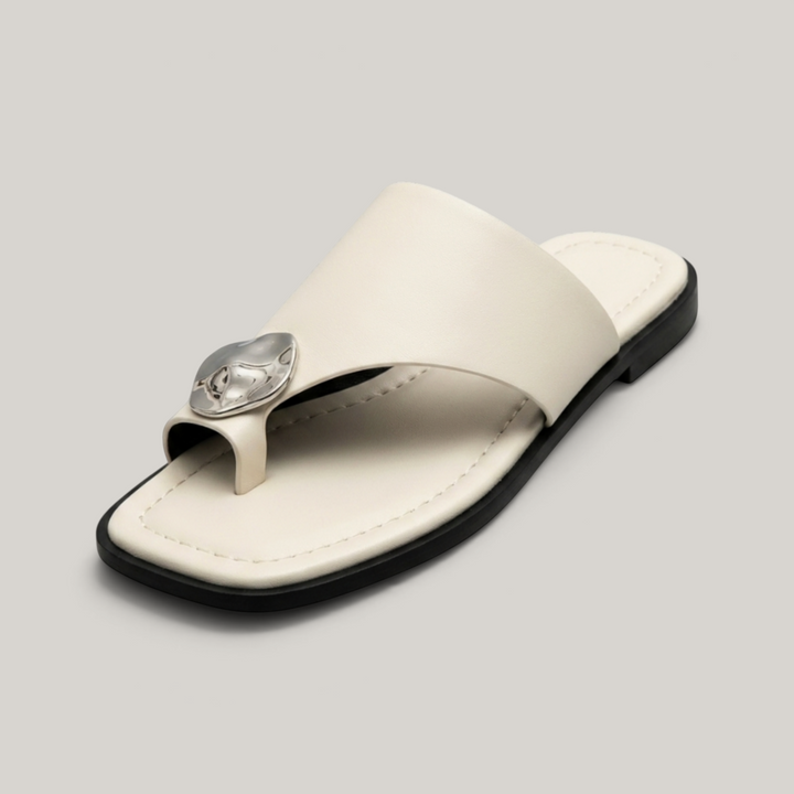 Cleo Sandal in Ivoire Argenté. Single wide ivory leather band, molten silver medallion, toe-ring thong construction on flat black sole.