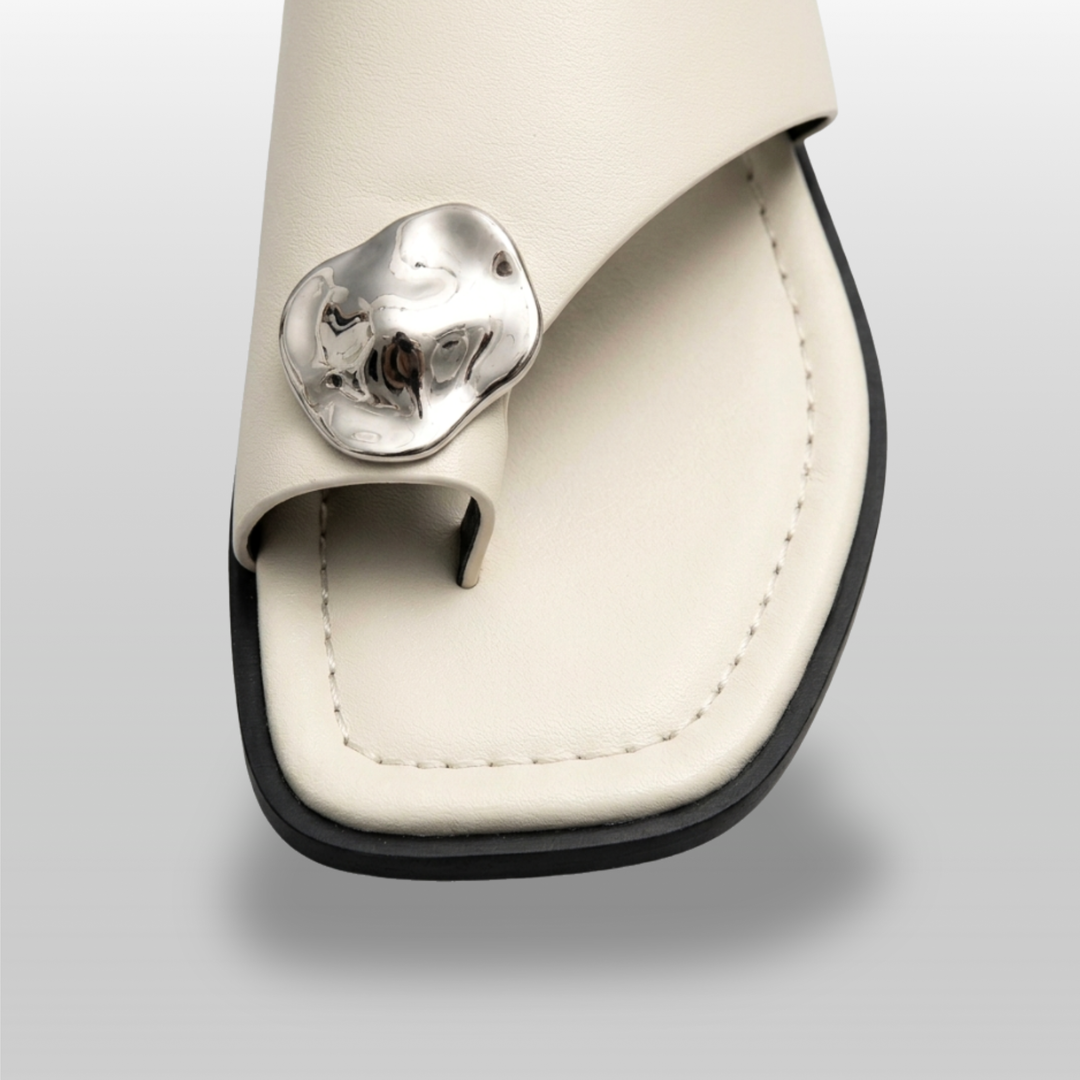 Cleo Sandal in Ivoire Argenté. Close detail of the molten silver medallion — organic irregular form, hammered artisan-cast finish.