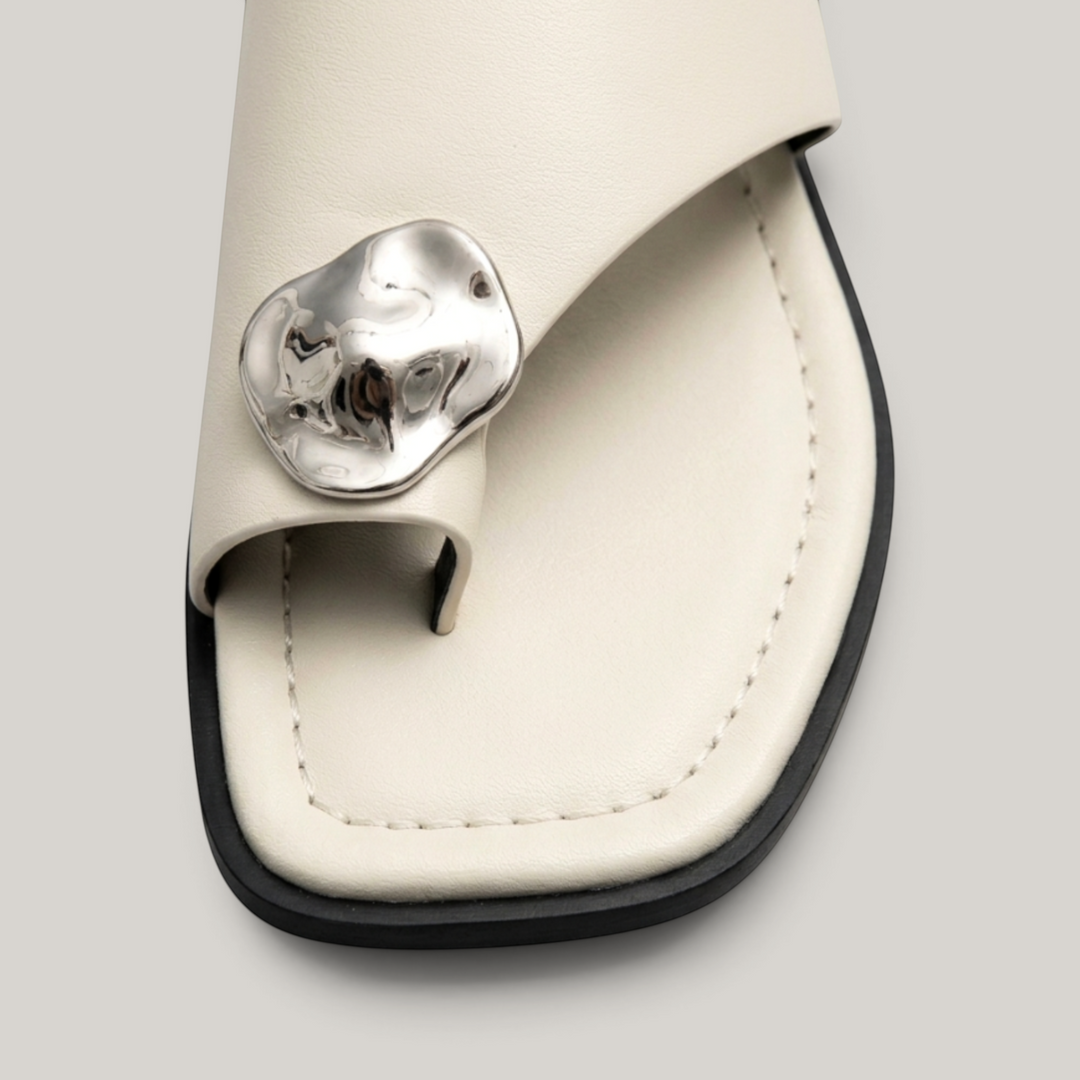 Cleo Sandal in Ivoire Argenté. Close detail of the molten silver medallion — organic irregular form, hammered artisan-cast finish.