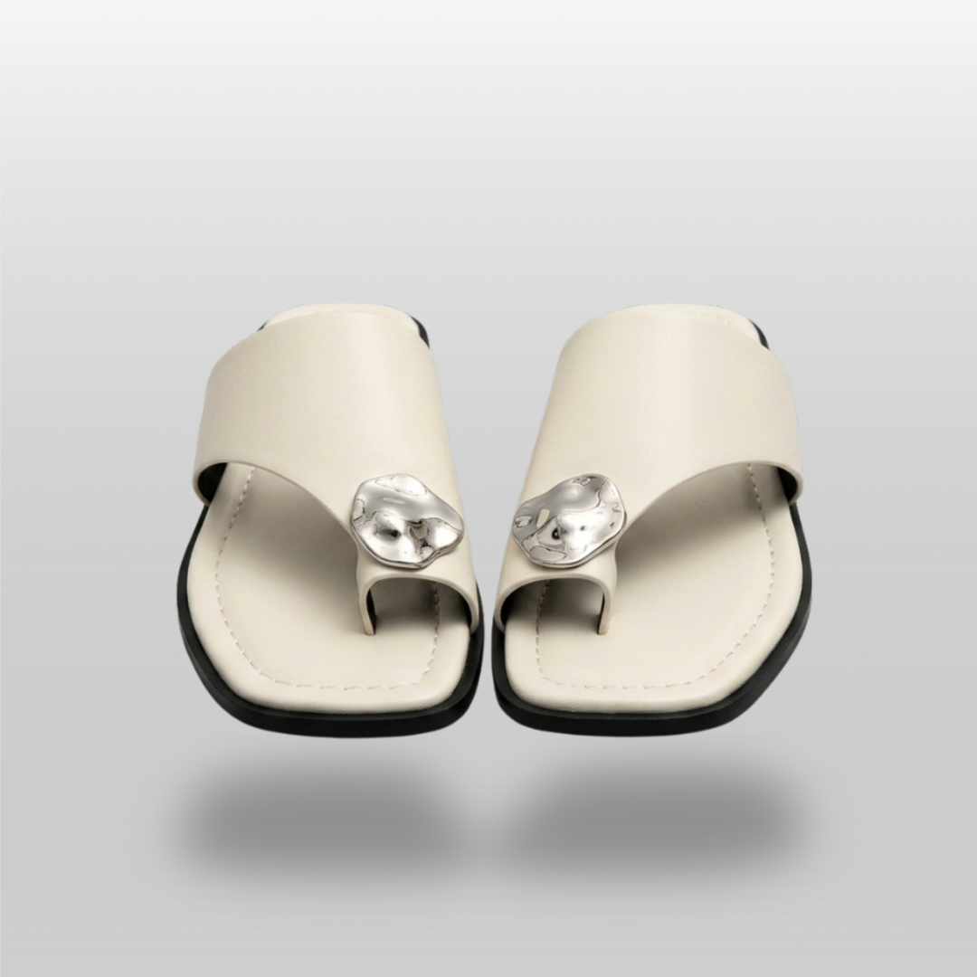 Cleo Sandal in Ivoire Argenté. Pair of flat ivory leather toe-ring sandals with molten silver medallion accent.