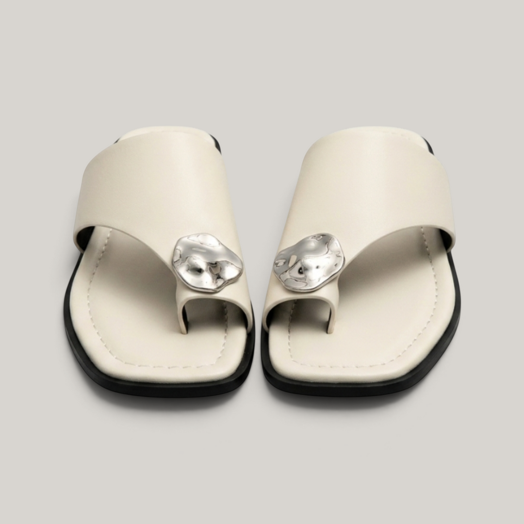 Cleo Sandal in Ivoire Argenté. Pair of flat ivory leather toe-ring sandals with molten silver medallion accent.