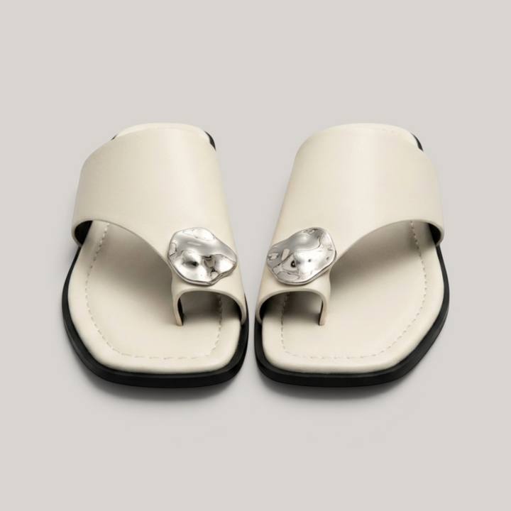 Cleo Sandal in Ivoire Argenté. Pair of flat ivory leather toe-ring sandals with molten silver medallion accent.