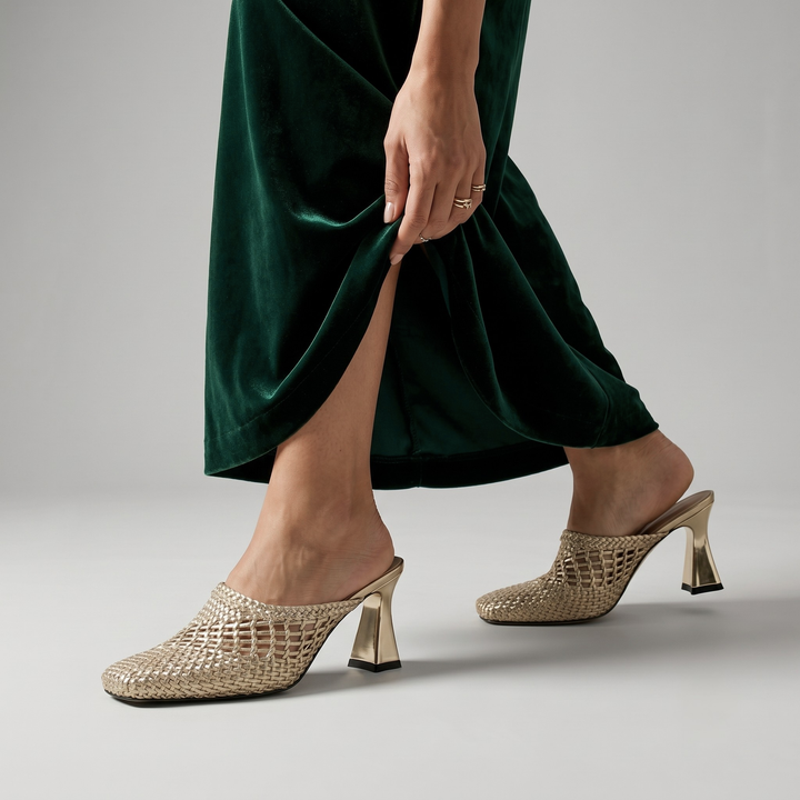 Metallic gold Dorée Mule heels with a braided woven upper and square toe, styled with a dark green velvet dress.