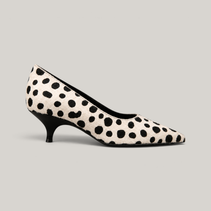 Side profile of spotted ivory pump showing curved black kitten heel