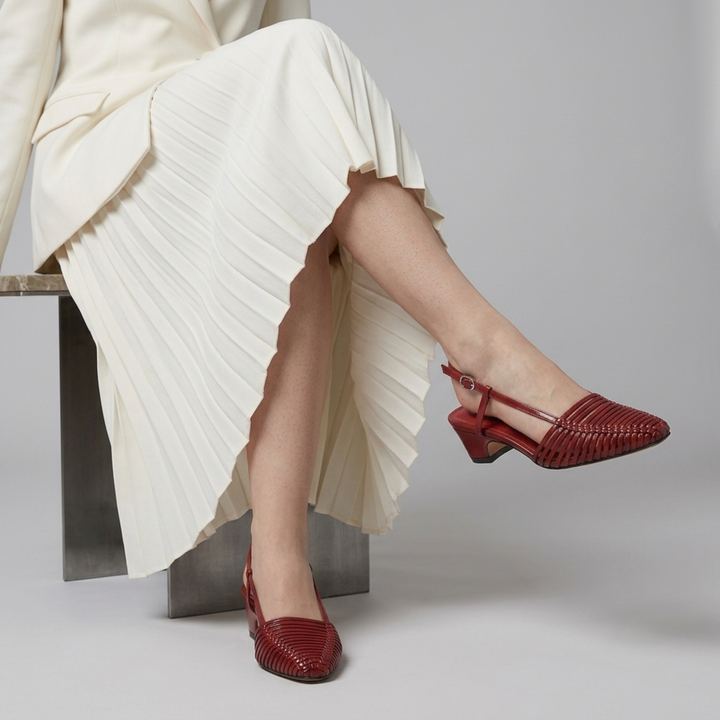 Close-up of a model wearing the Margot woven leather slingback shoes in Rouge Claret, styled with a flowing cream pleated skirt.
