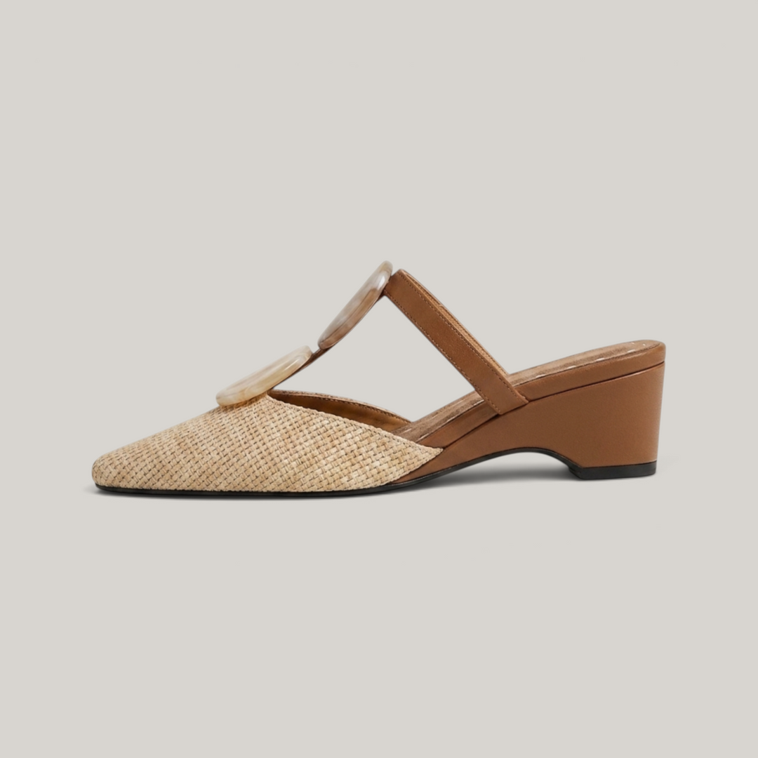 Paloma Mule in Sable Doré. Lateral silhouette showing the soft square toe, raffia upper, resin medallions and continuous camel wedge.