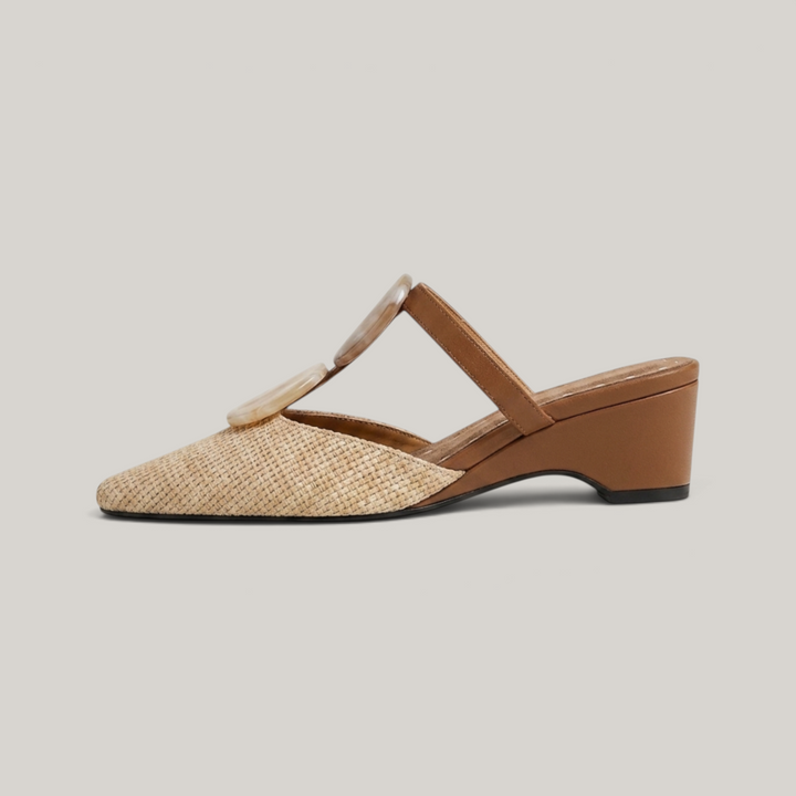 Paloma Mule in Sable Doré. Lateral silhouette showing the soft square toe, raffia upper, resin medallions and continuous camel wedge.
