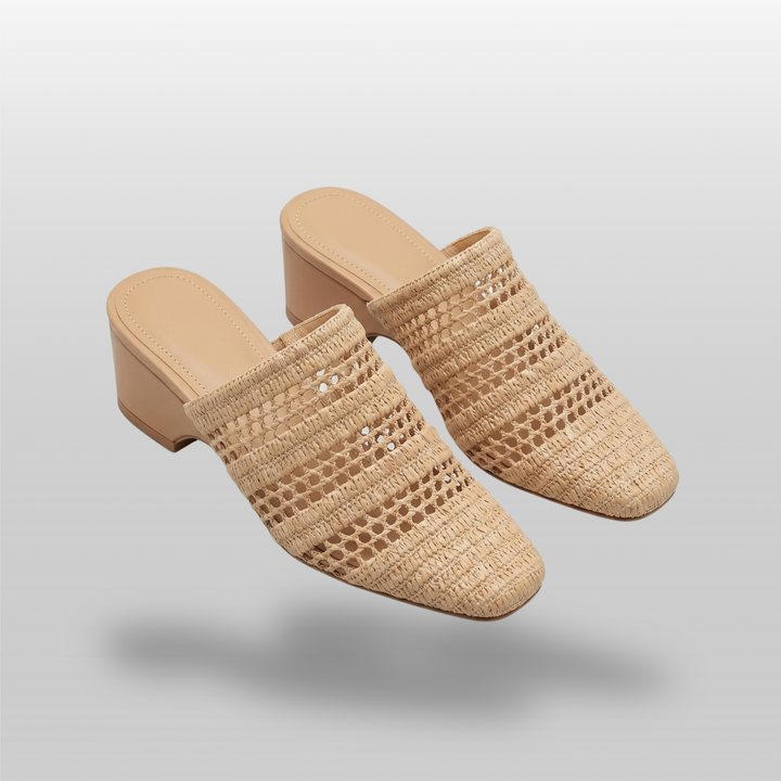 A pair of Riviera Mules in Sable Naturel highlighting the natural woven raffia texture and elegant open-back construction.