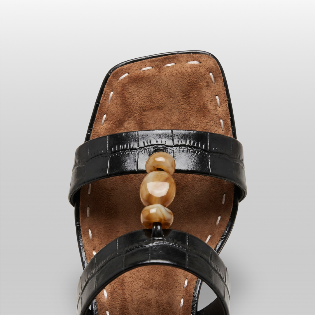 Sculpture Sandal in Noir Croco. Close detail of hand-strung amber resin beads on crocodile-embossed leather.