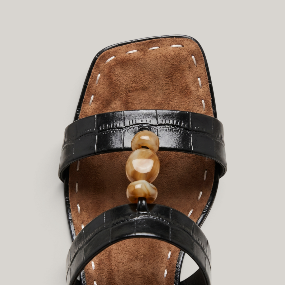 Sculpture Sandal in Noir Croco. Close detail of hand-strung amber resin beads on crocodile-embossed leather.