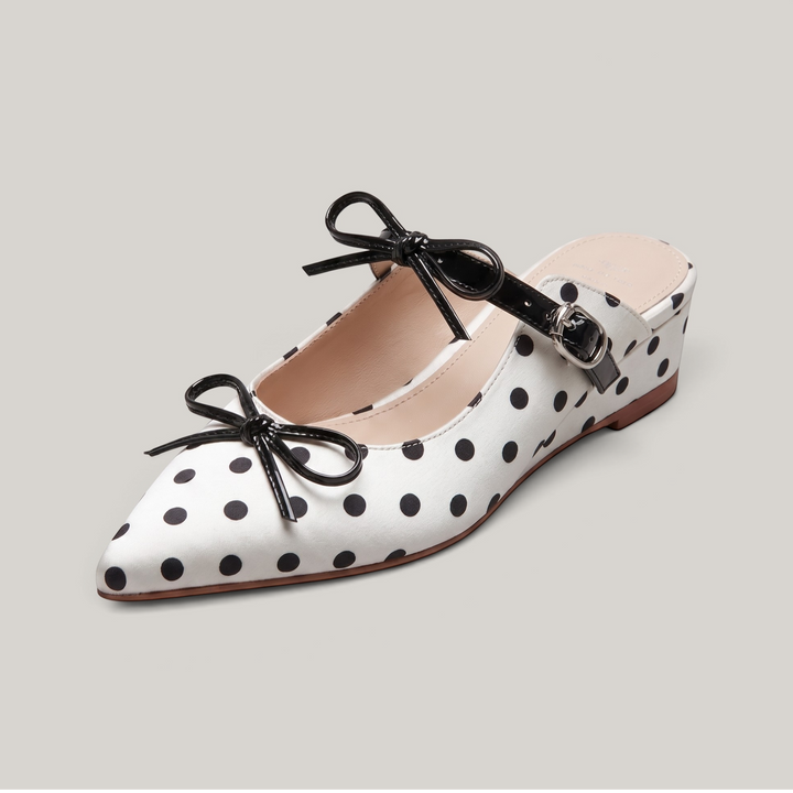USS® Shoes Elise pointed-toe mule in white leather with black polka dots, featuring black bow accents and buckle strap.