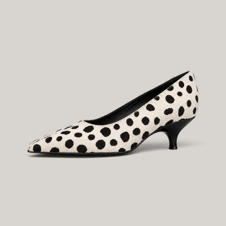 USS® Shoes Manon pump in ivory hair-on leather with black irregular spots, pointed toe, and curved kitten heel.